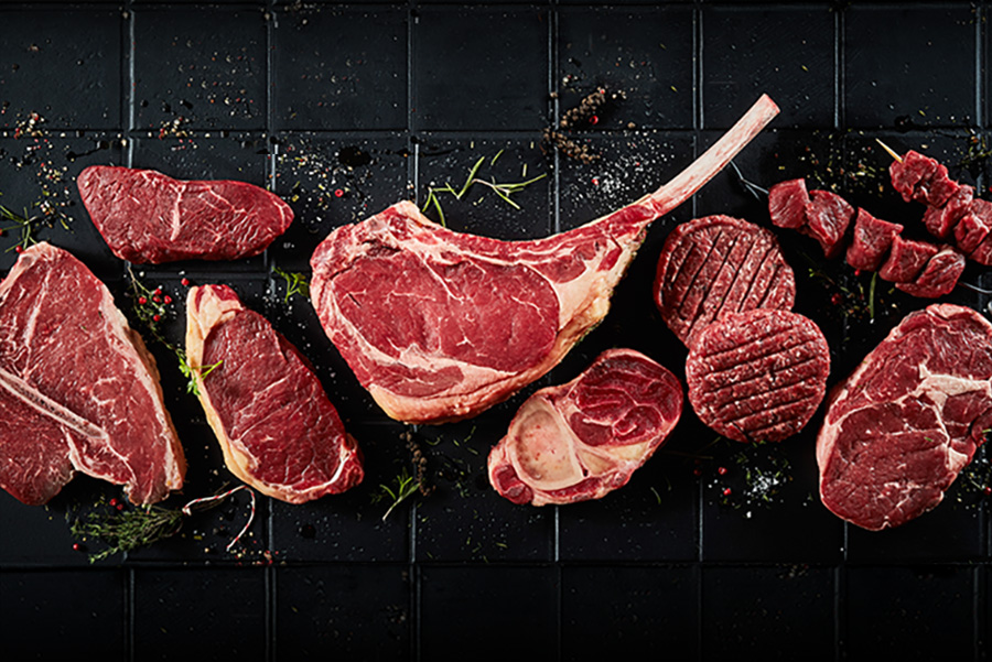 beef steaks, cutlets, and shish kabobs seasoned on a black tile countertop