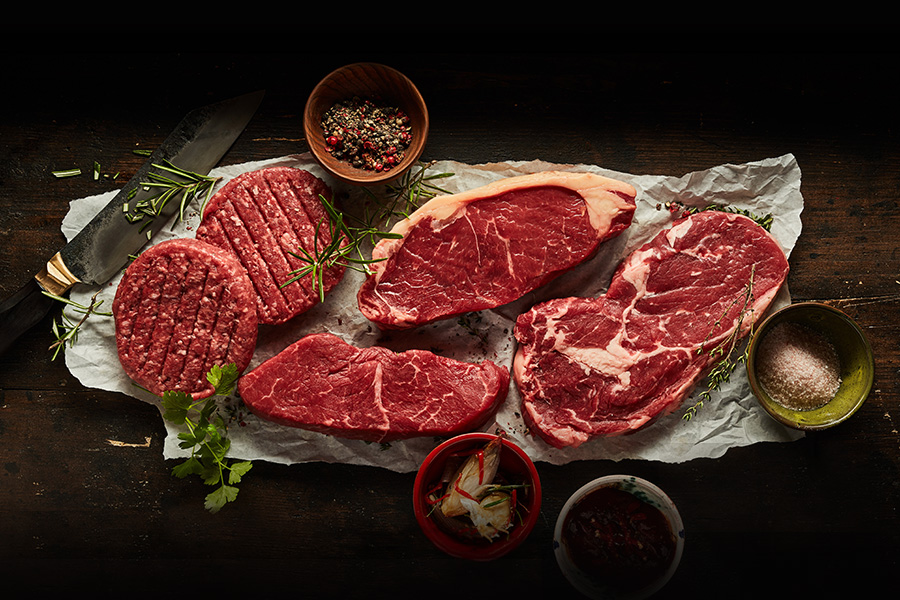 beef steaks, cutlets, burgers, and knife seasoned on parchment paper and a wood slab