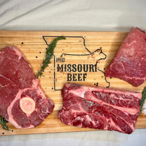 Three slabs of beef sitting on a cutting board with herbs and spices, cutting board reads Mid Missouri Beef