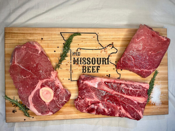 Three slabs of beef sitting on a cutting board with herbs and spices, cutting board reads Mid Missouri Beef