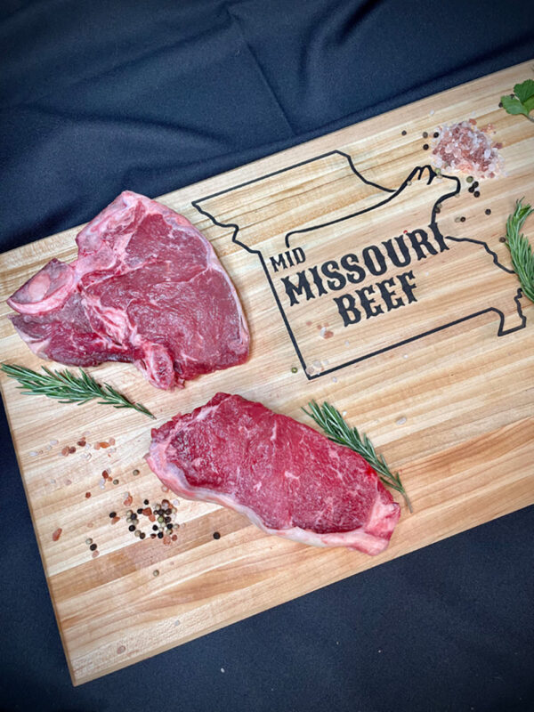 two slabs of steak on a cutting board with herbs and spices, cutting board reads Mid Missouri Beef